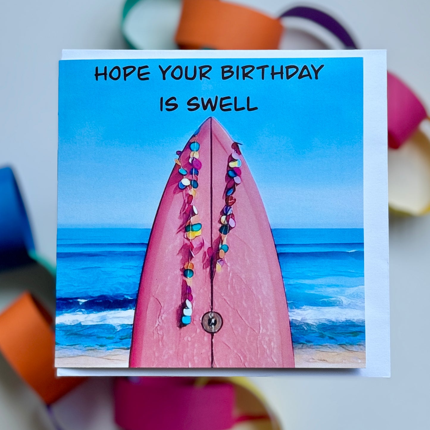greeting card with a pink surfboard with the surf beach in the background
