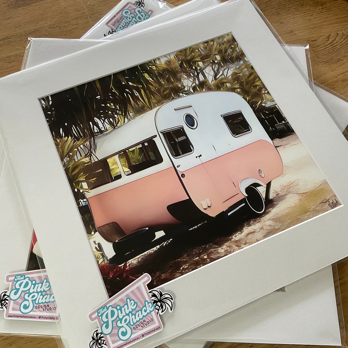 A pink and white vintage bondwood caravan with some trees surrounding it print With a white mat in a clear poly bag