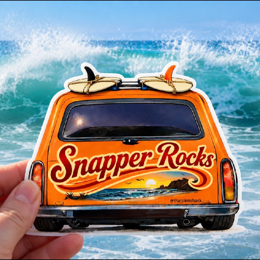 A hand holds a die-cut sticker shaped like the back of an orange holden panel van with surfboards on the roof and large 'Snapper Rocks' lettering, set against a real ocean wave background.
