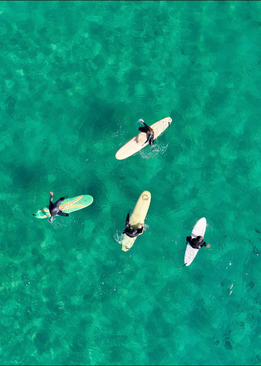 Four surfers sitting on their boards in clear green water