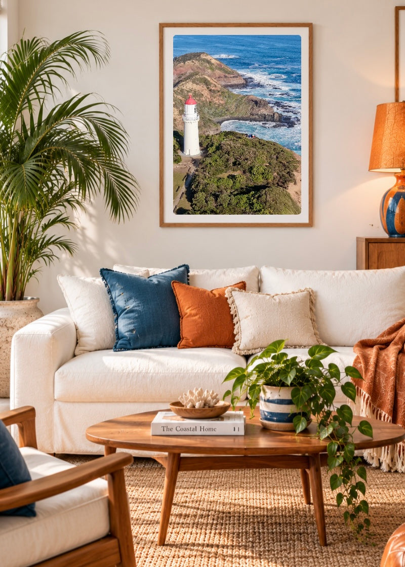 Cape Schanck Lighthouse coastal print displayed in a timber frame above a white sofa in a retro-inspired lounge room with blue and orange accents.