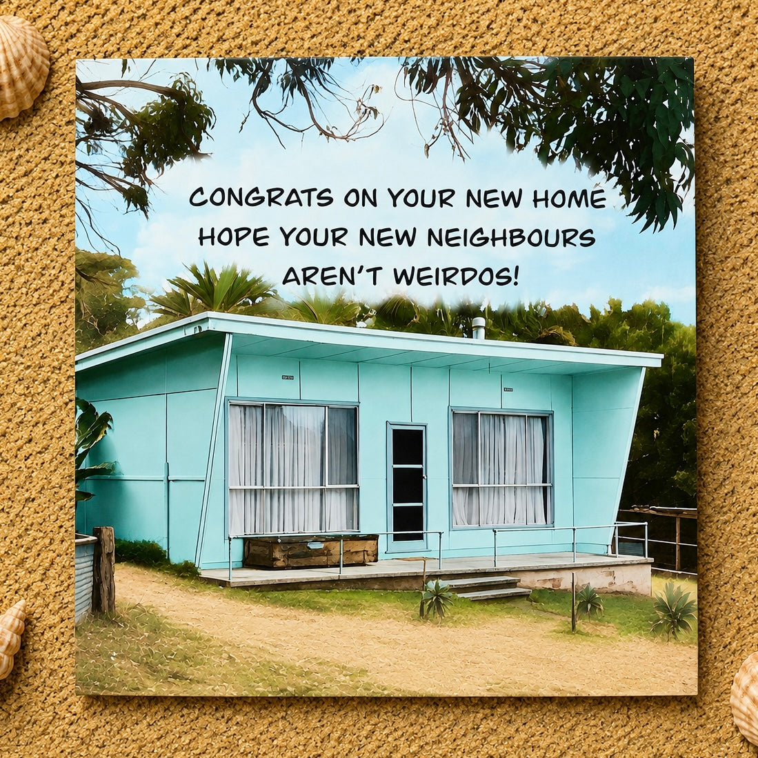 A square greeting card featuring a photo of a light aqua single-story house with the text 'CONGRATS ON YOUR NEW HOME HOPE YOUR NEW NEIGHBORS AREN'T WEIRDOS!' in black lettering. The card is centered on a textured sand background with small shell decorations in the corners.