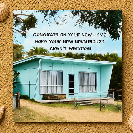 A square greeting card featuring a photo of a light aqua single-story house with the text 'CONGRATS ON YOUR NEW HOME HOPE YOUR NEW NEIGHBORS AREN'T WEIRDOS!' in black lettering. The card is centered on a textured sand background with small shell decorations in the corners.