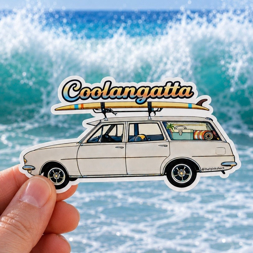 A hand holds a die-cut sticker featuring an illustrated white holden surf wagon with a surfboard on its roof and the word 'Coolangatta' above it, set against an ocean wave background.