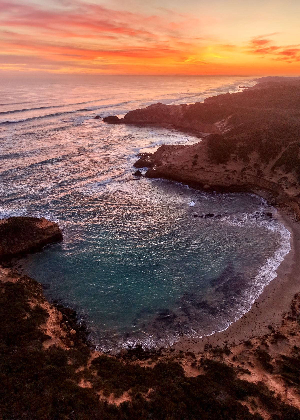 Aerial drone photograph of Diamond Bay, Sorrento at sunset showing turquoise ocean, sandy beach, rugged cliffs and the Mornington Peninsula coastline.
