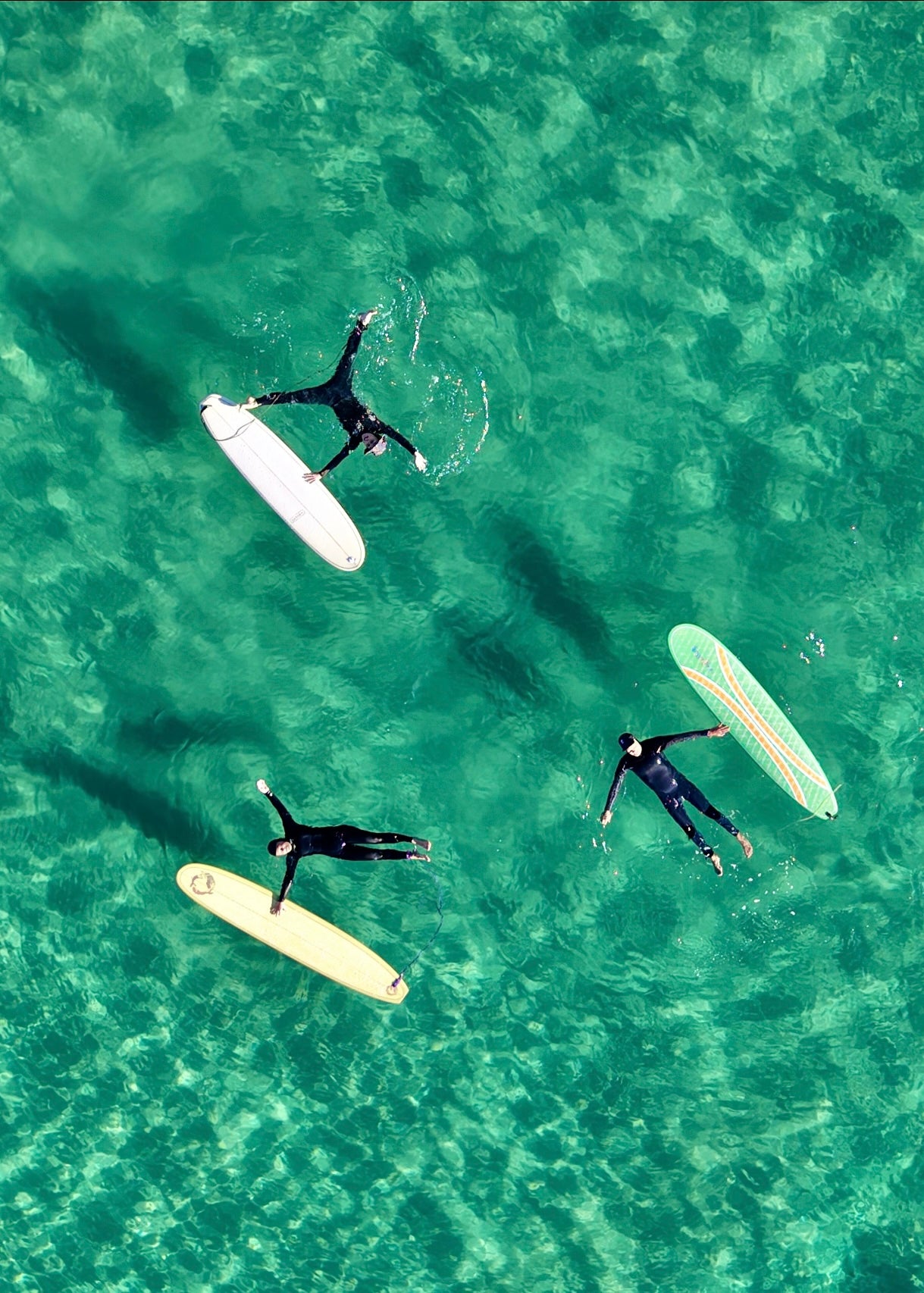 Three surfers laying starfish style in the clear Green water next to their surfboards