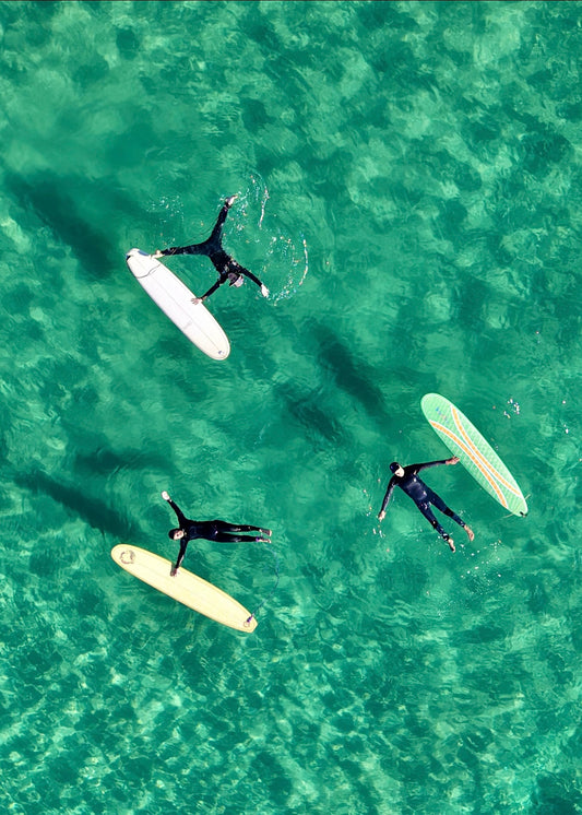 Three surfers laying starfish style in the clear Green water next to their surfboards
