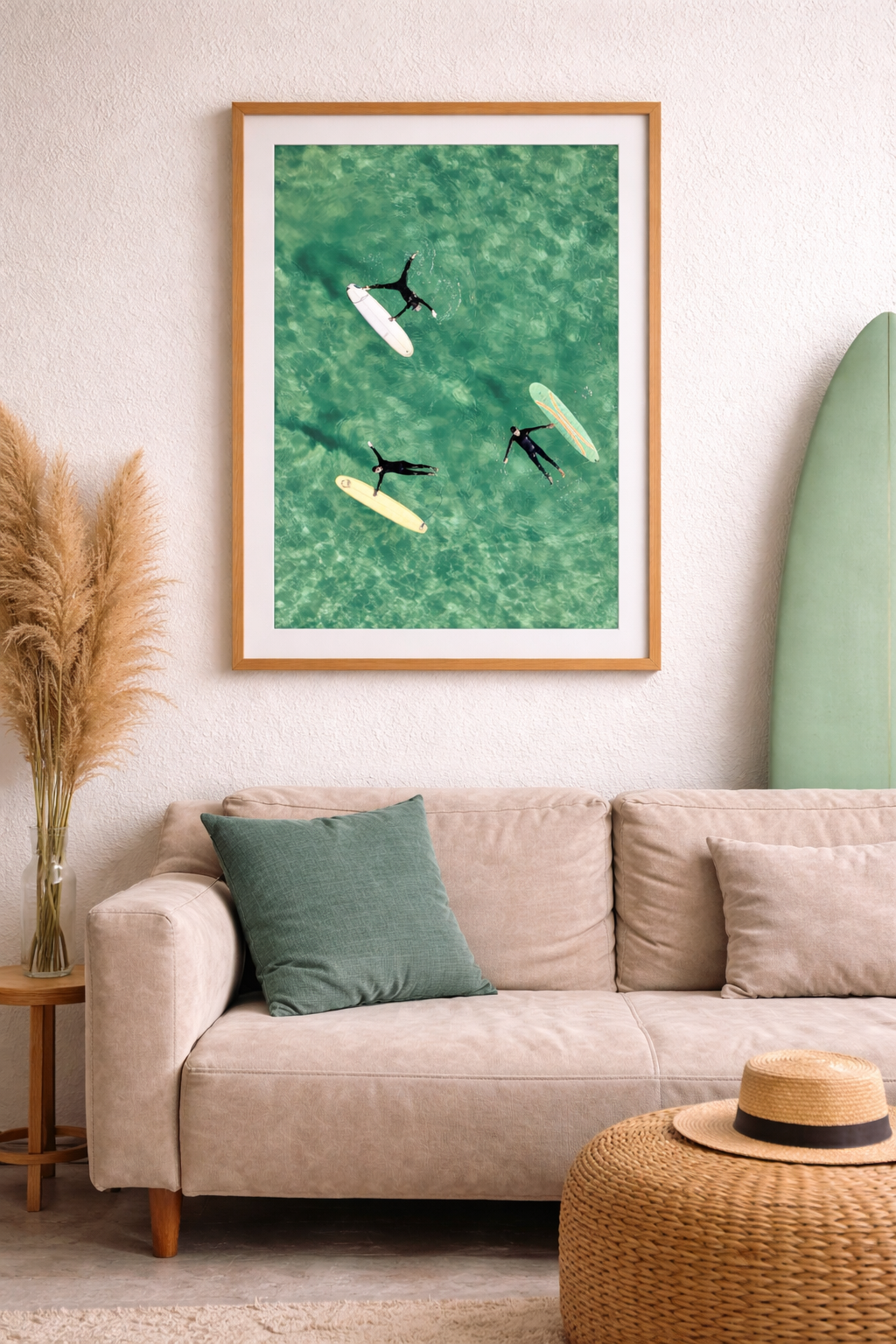 Framed artwork of surfers in the water above surfboards leaning on a wall above a beige sofa.