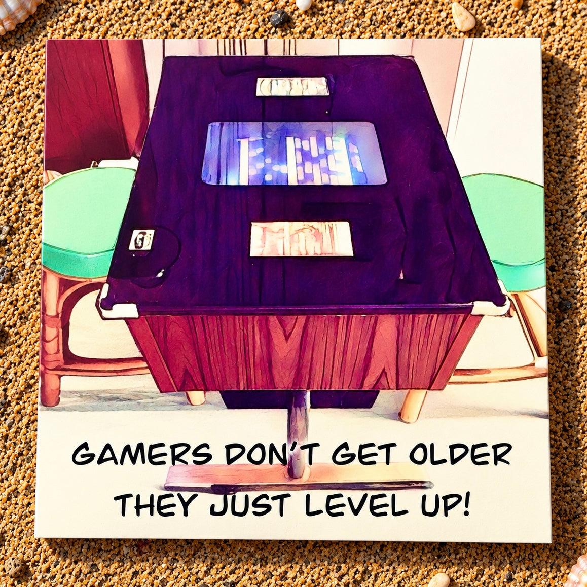 A square greeting card featuring a humorous gaming-themed design. The top half shows a stylized, colorful illustration of a wooden retro sit down arcade gaming table with a dark purple felt surface and glowing blue lights, flanked by mint green stools. With the text Gamers don’t get older they just level up