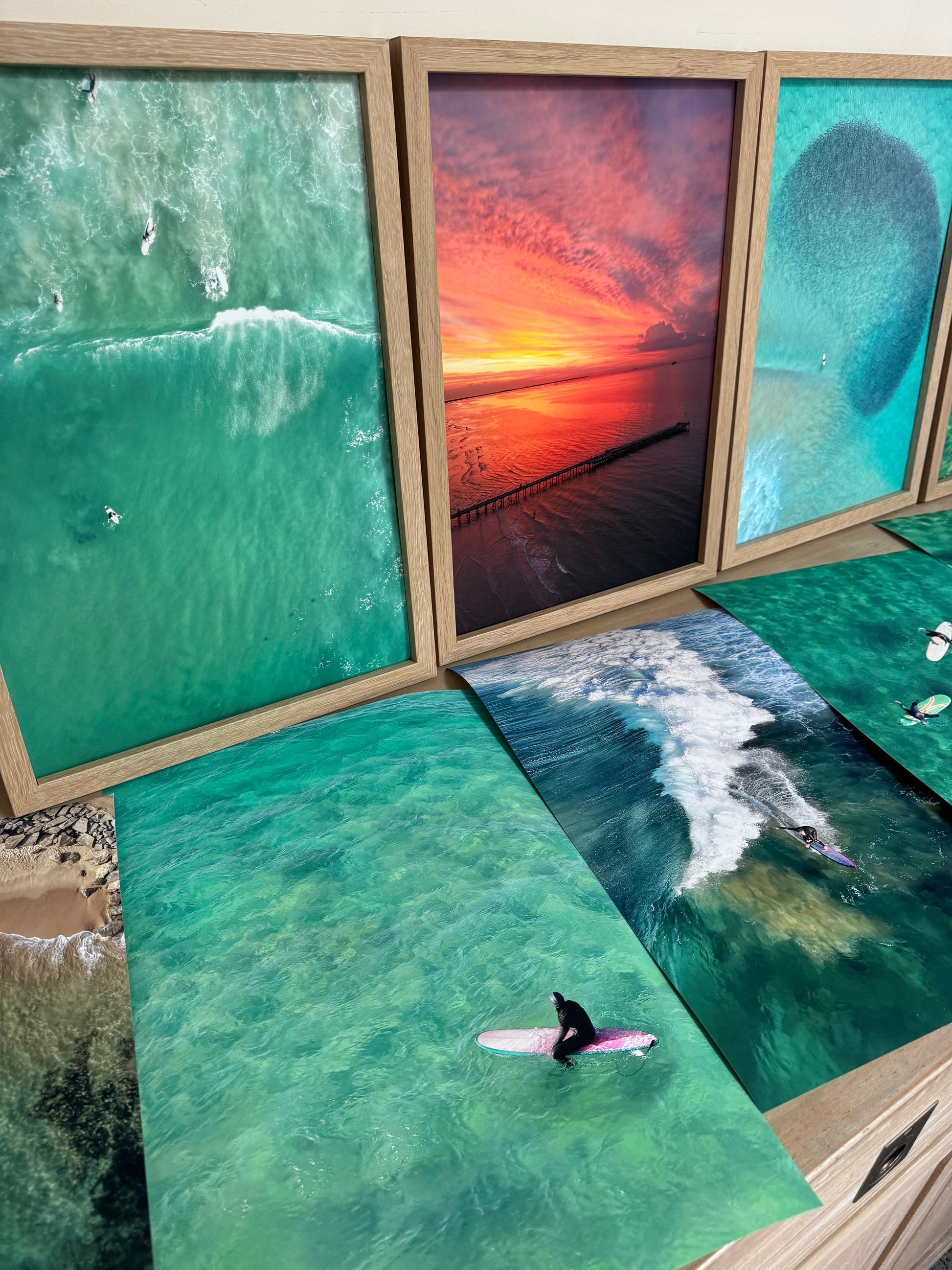 Set of framed and Unframed  beach-themed artworks including ocean waves , sunset . surfers and boats