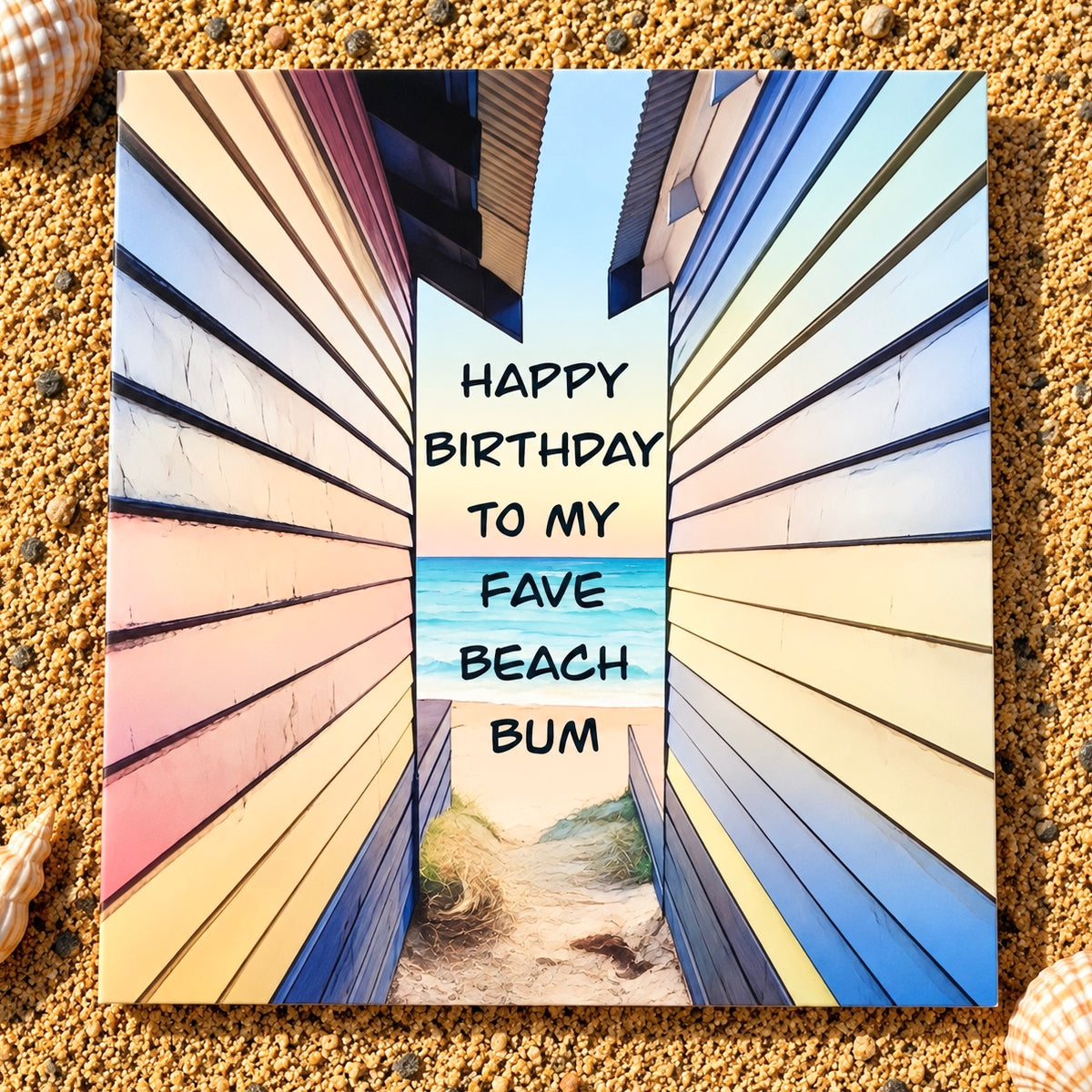 A square printed greeting card featuring a colorful perspective view of beachside wooden cabanas with a central beach and ocean scene, overlaid with the text 'HAPPY BIRTHDAY TO MY FAVE BEACH BUM'. The card is displayed flat on a sandy surface with seashells in the corners.