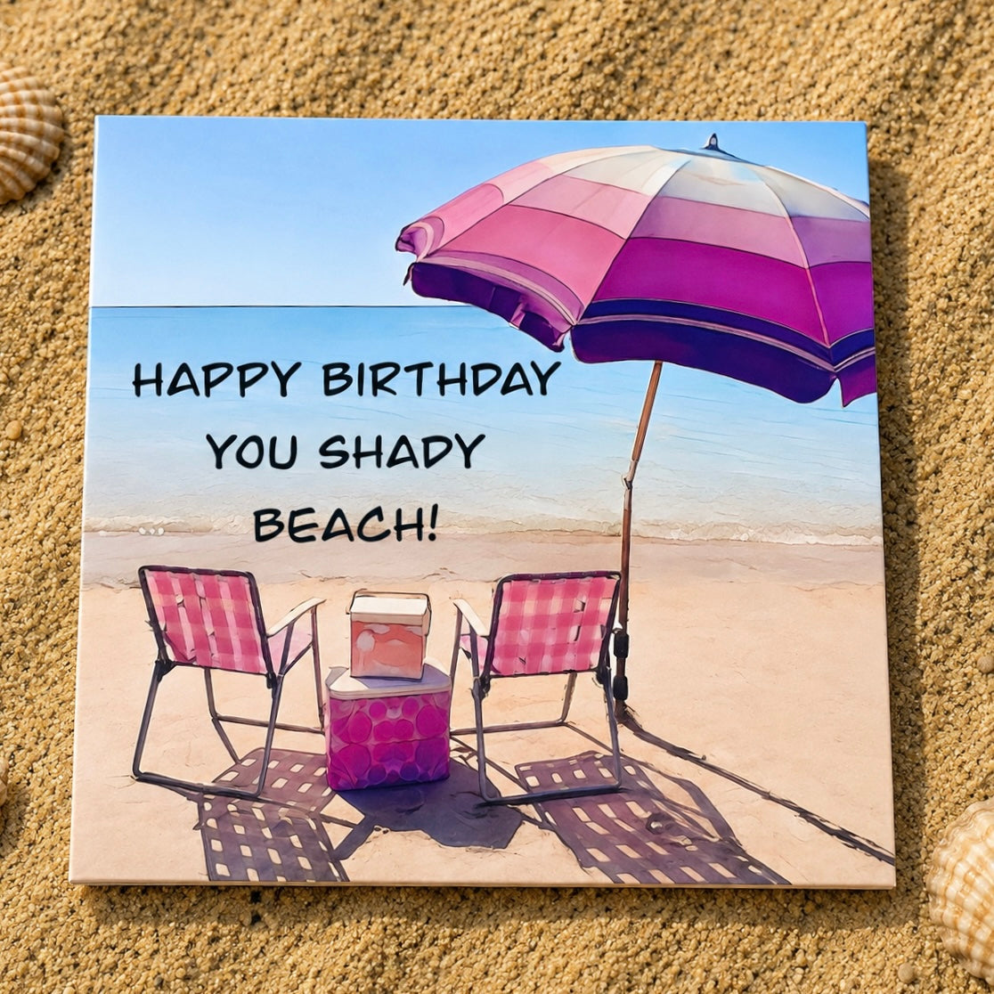 A square greeting card featuring a beach scene with two pink lounge chairs, a pink and purple striped umbrella, and a small cooler, with the text 'HAPPY BIRTHDAY YOU SHADY BEACH!' printed on it. The card is displayed flat on a bed of sand