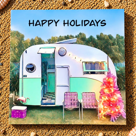A square holiday greeting card featuring a retro travel trailer in a grassy outdoor setting with the words “HAPPY HOLIDAYS” at the top. The trailer is white and mint green, with two pink patio chairs in front and a pink tropical tree on the right.