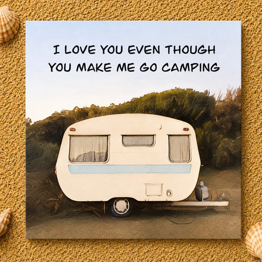 Square greeting card featuring a vintage cream and light blue camping caravan parked outdoors with the text 'I LOVE YOU EVEN THOUGH YOU MAKE ME GO CAMPING' above it, displayed on a sandy textured background with small seashell accents.