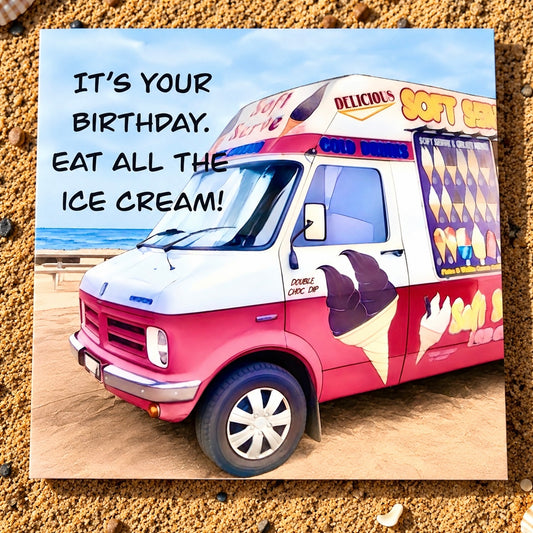 A square printed greeting card featuring a beach scene with an ice cream truck and the text 'IT'S YOUR BIRTHDAY. EAT ALL THE ICE CREAM!' placed on a sandy surface.