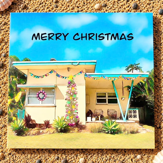 A primed quare Christmas greeting card featuring a vintage yellow beach shack with Christmas tree and a pink wreath on the window 