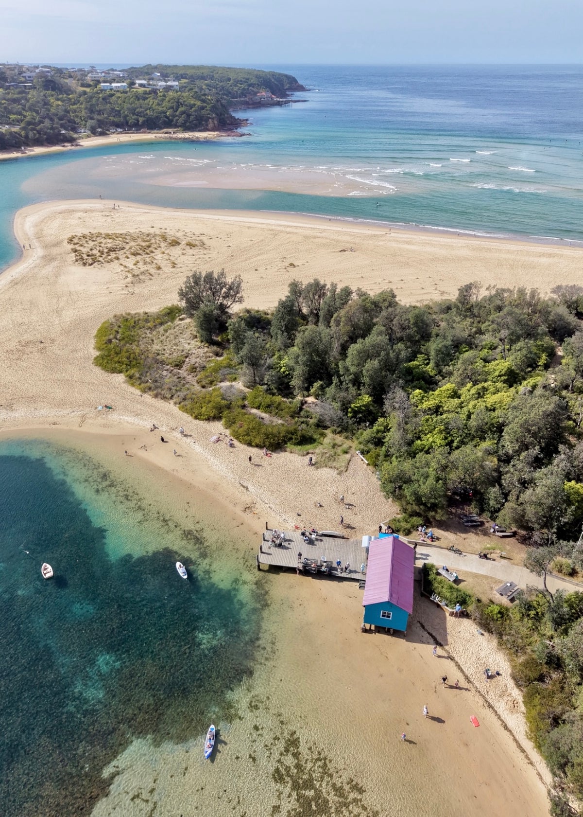 Aerial drone view of Mitchies Jetty in Merimbula, Sapphire Coast NSW, with turquoise water, sandy beach and coastline.