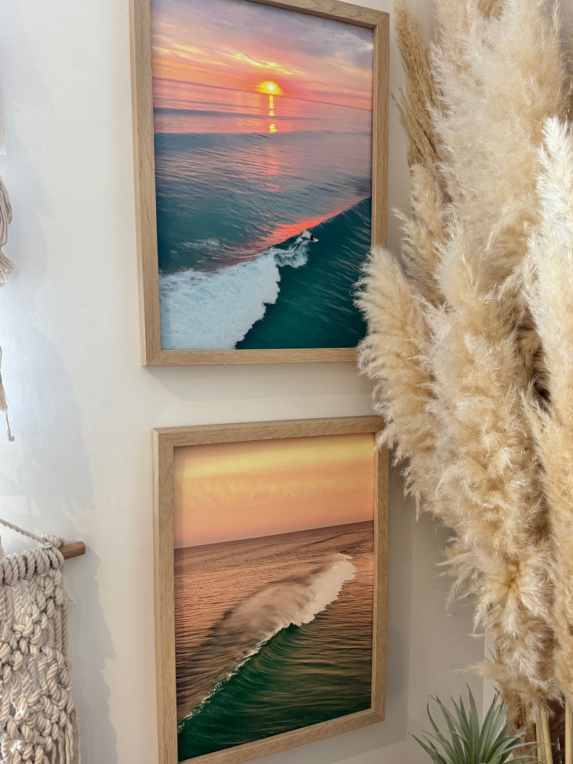 Two framed artworks of ocean scenes on a wall with pampas grass.
