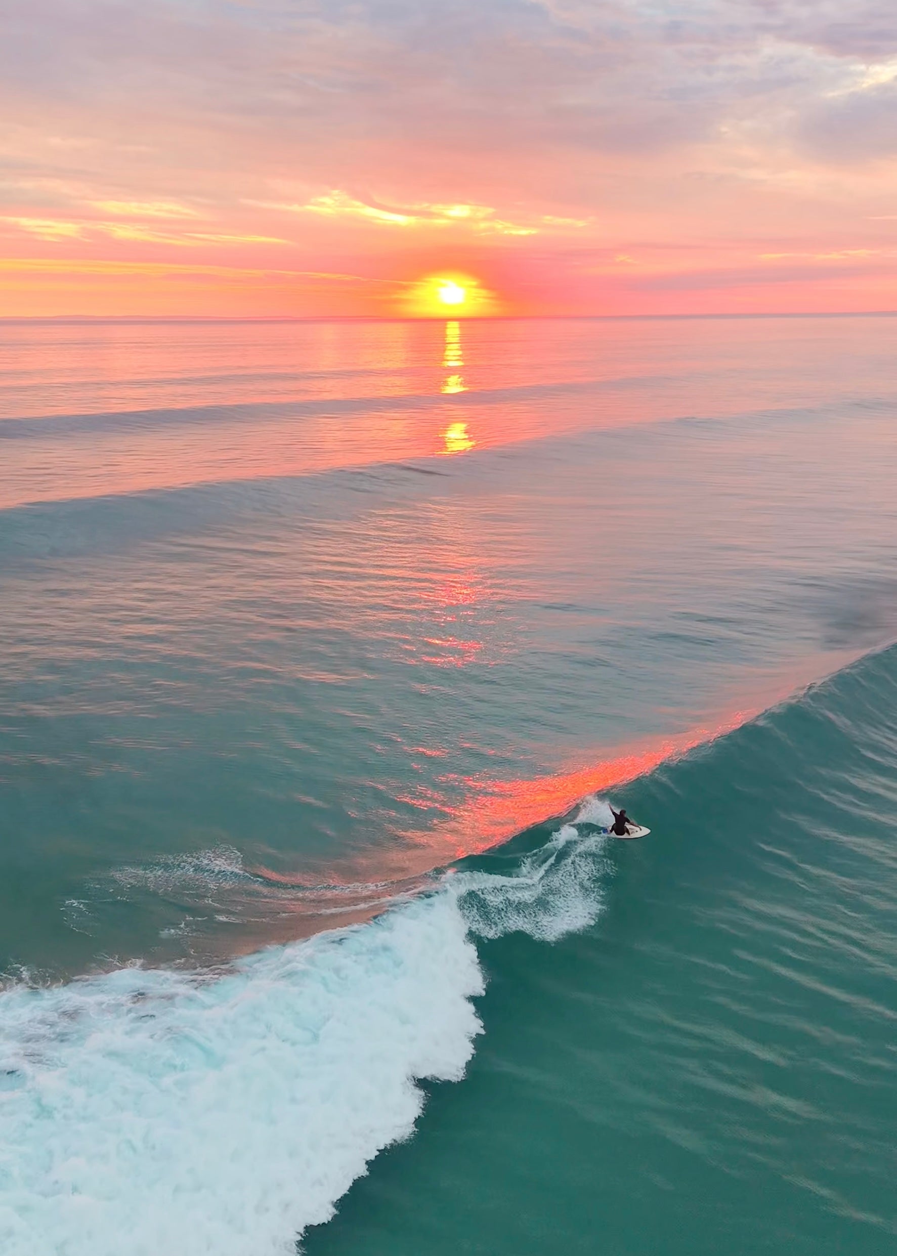 A perfect night with the sun setting ver the water and a surfer catching a perfect glassy peeling wave