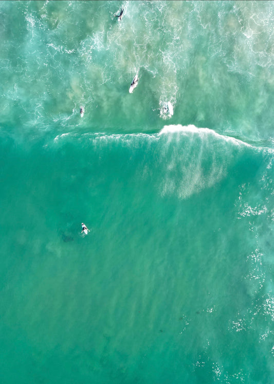 Aerial view of people surfing on a wave in clear blue water.