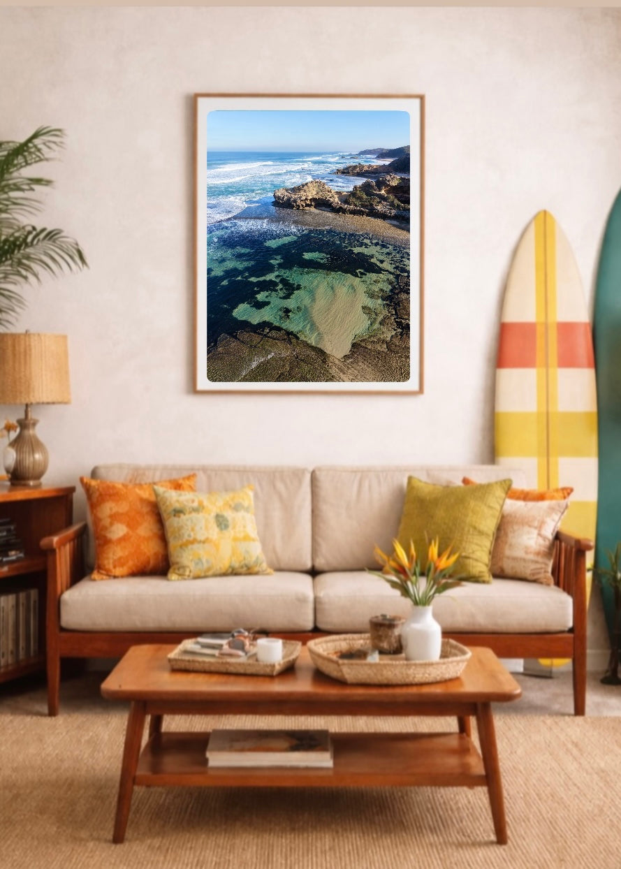 Portsea Back Beach coastal print displayed in a timber frame above a retro-style sofa with colourful cushions and surfboards.