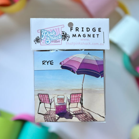 A fridge magnet of rye beach with pink camp chairs and a vintage umbrella in packaging