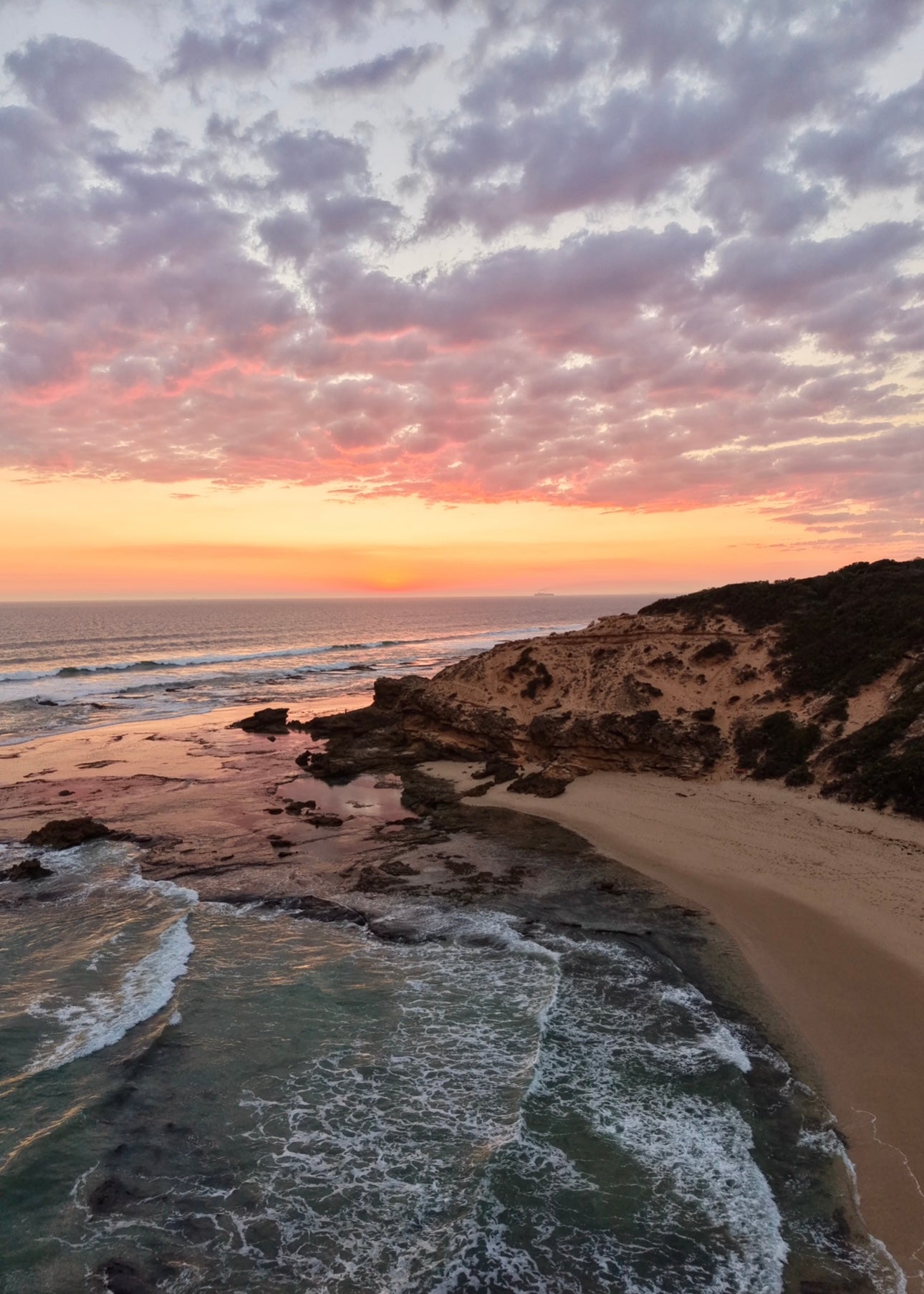 Sunset over Sorrento  beach with rockpools , rock formations , sand  and waves.