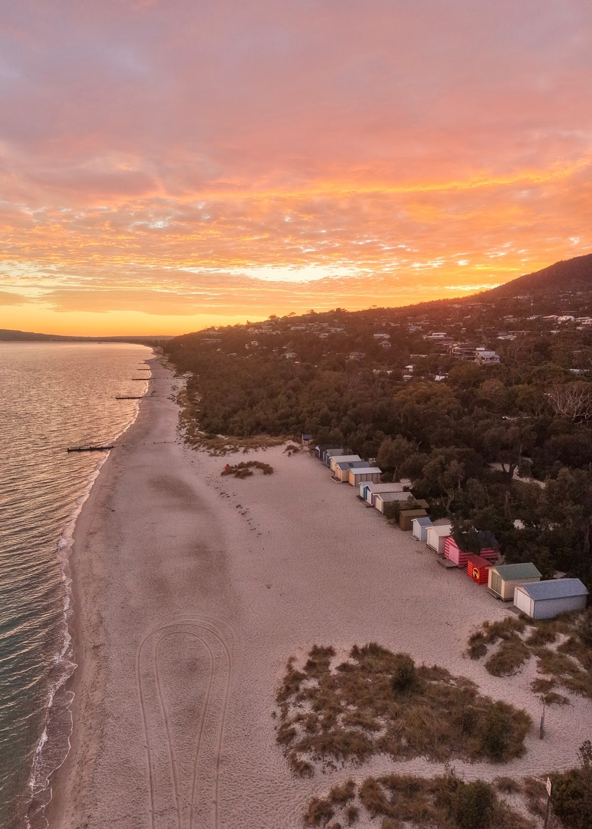 An aerial photo of Beach scene with beach boxes, white sand, clear water and a colorful sunrise sky