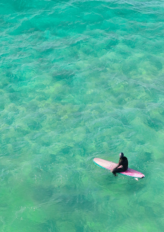 Solo surfer girl on a pink surfboard in clear turquoise water
