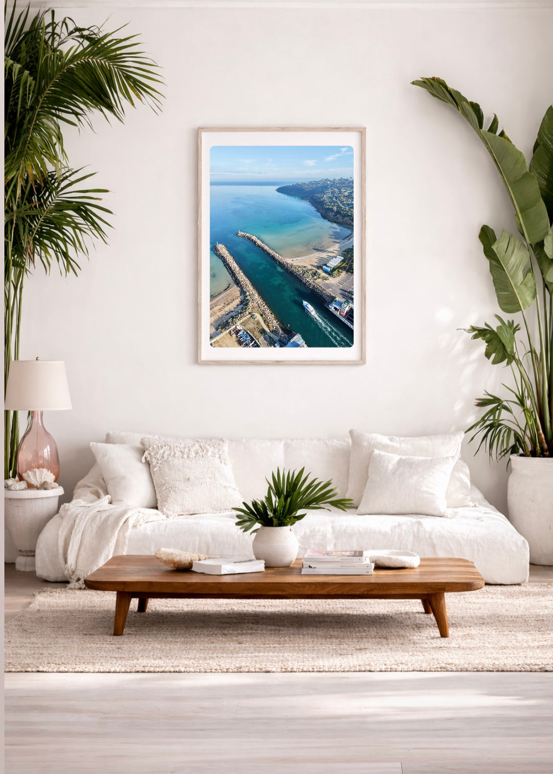 Living room with a large framed picture of Tassells_Cove_Safety_beach_Martha_Cove_drone_print, white sofa, wooden coffee table, and plants.