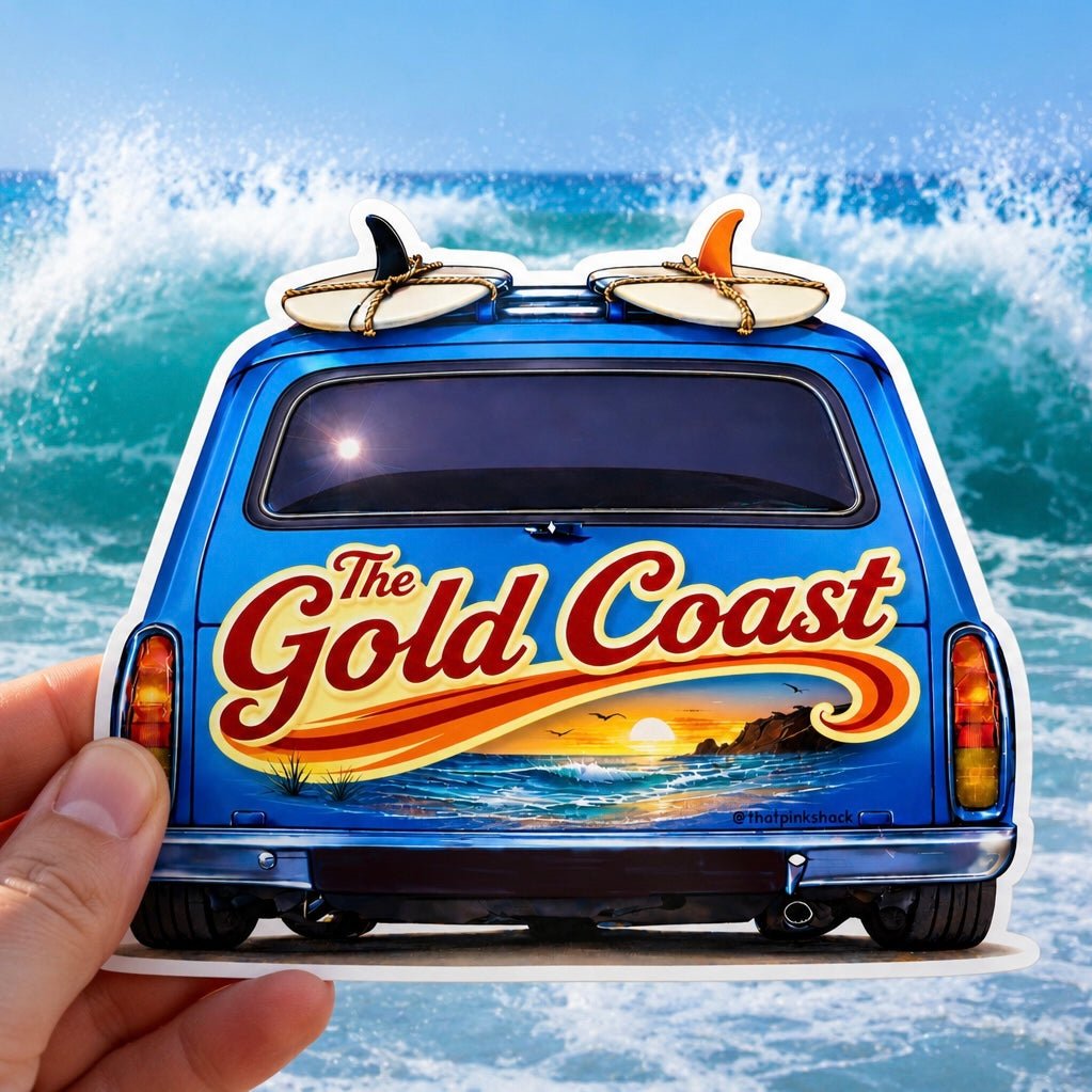 A die-cut sticker or decal shaped like the back of a blue sandman panel van with surfboards on top and large 'The Gold Coast' lettering over a beach sunset scene, held by a hand against a blue ocean wave background.