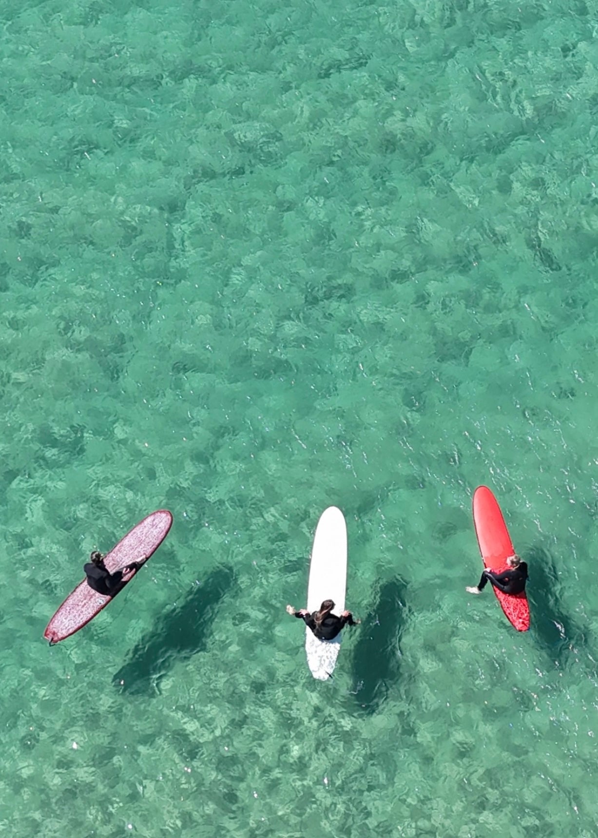 Three surfers in Tathra nsw sitting on their boards in clear turquoise water