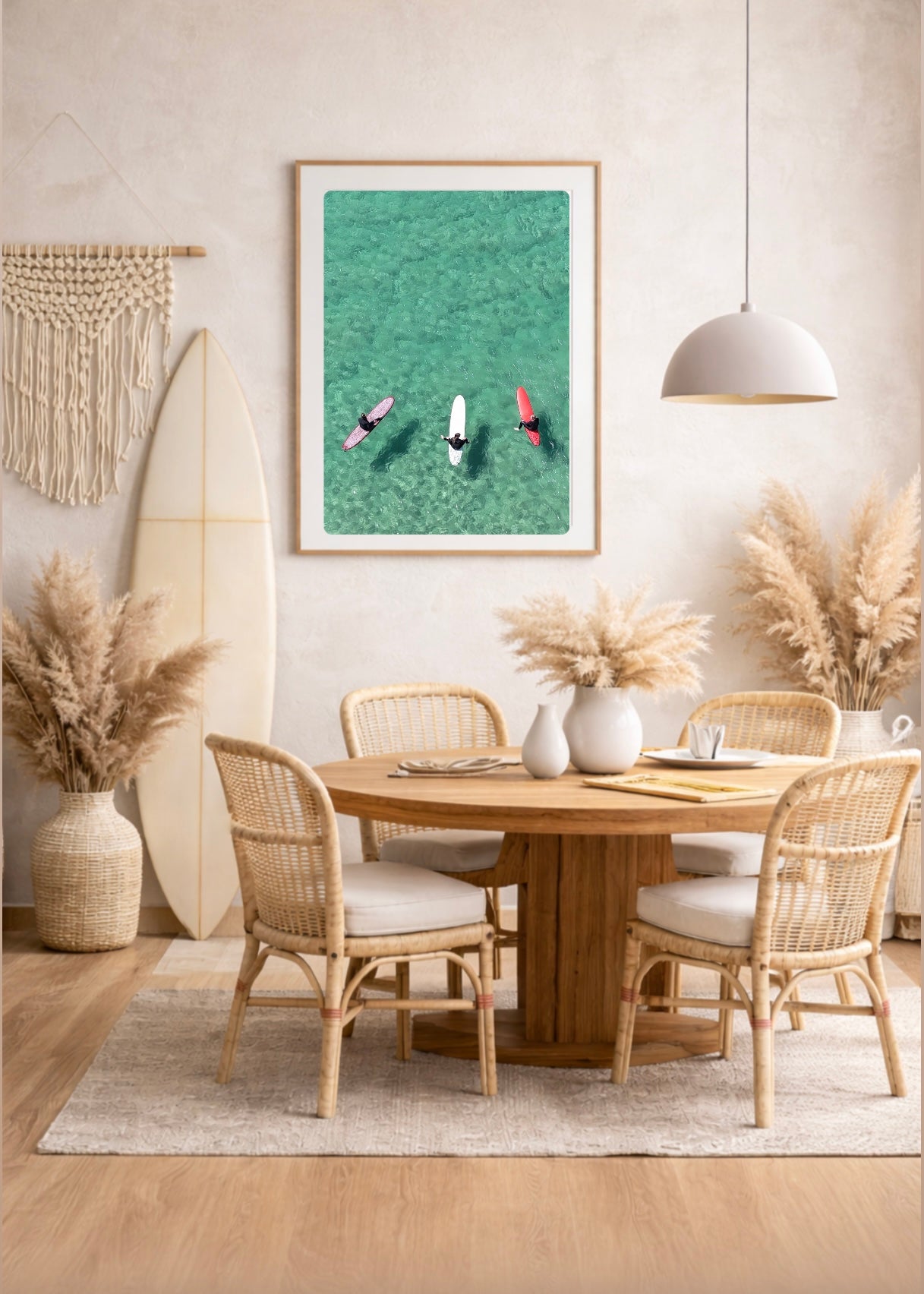 Dining room with wooden table, wicker chairs, and a surfboard against the wall with a framed print of three surfers in clear turquoise water