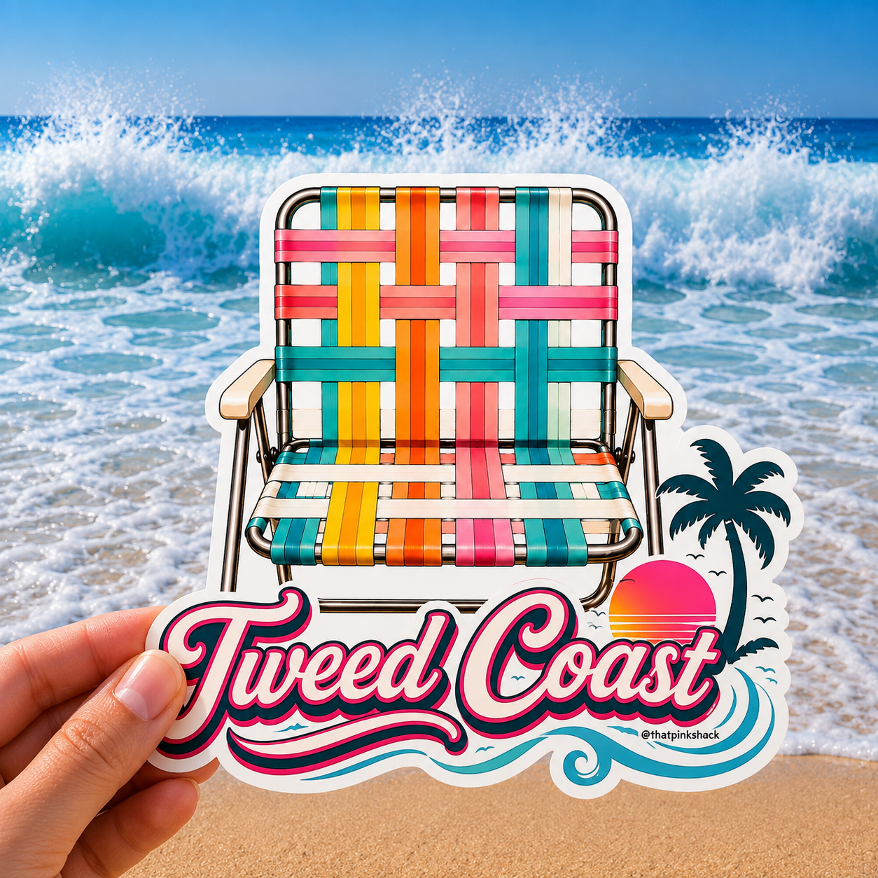 A hand holds a die-cut sticker featuring a colorful retro beach chair in front of a beach scene with ocean waves and a palm tree. The sticker includes the text 'Tweed Coast' 