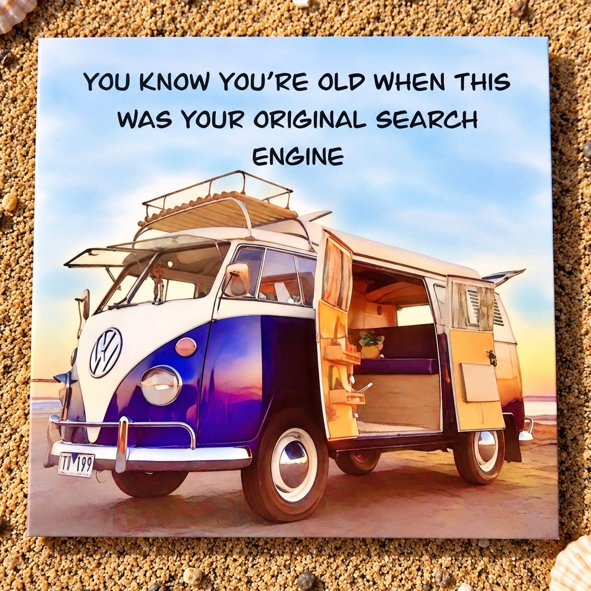 A square greeting card featuring a vintage blue and white Volkswagen camper van on a beach with the text 'YOU KNOW YOU'RE OLD WHEN THIS WAS YOUR ORIGINAL SEARCH ENGINE'. The card is displayed on a bed of sand and pebbles.