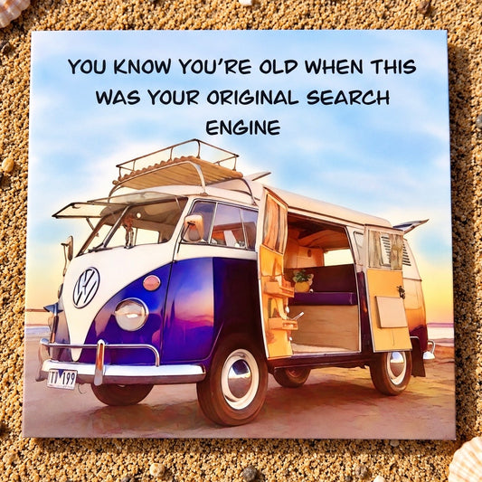 A square greeting card featuring a vintage blue and white Volkswagen camper van on a beach with the text 'YOU KNOW YOU'RE OLD WHEN THIS WAS YOUR ORIGINAL SEARCH ENGINE'. The card is displayed on a bed of sand and pebbles.